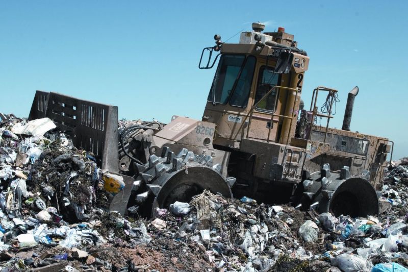 L'immagine ritrae un compattatore in azione su una montagna di rifiuti all'interno di una discarica